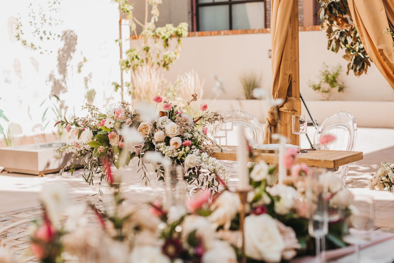 A close up of fa flower arrangement with candles on a table set for a bride and groom