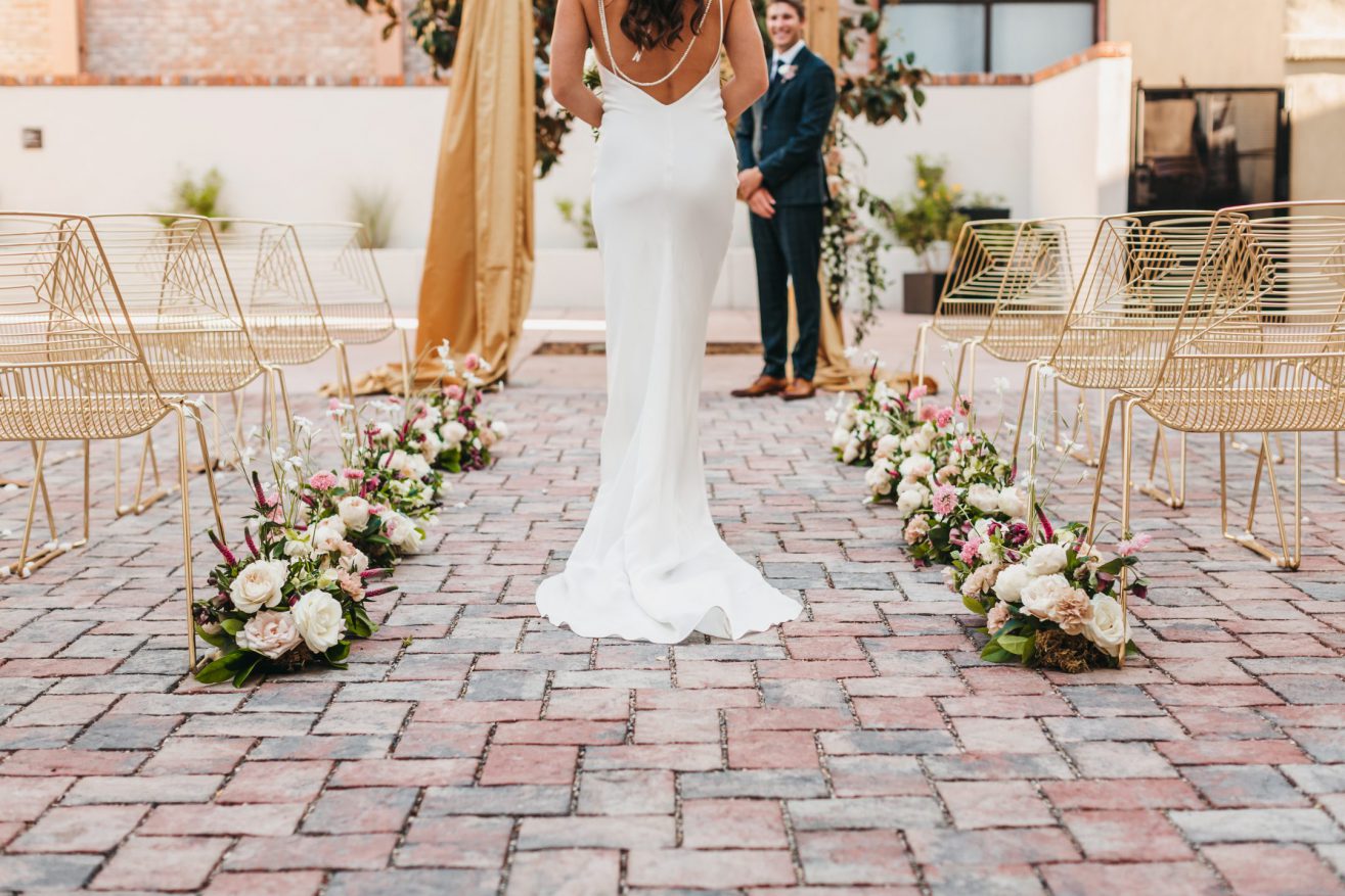 A bride walking toward the groom down the aisle lined with flowers