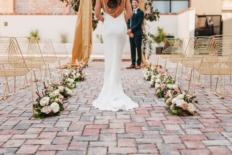 A bride walking toward the groom down the aisle lined with flowers