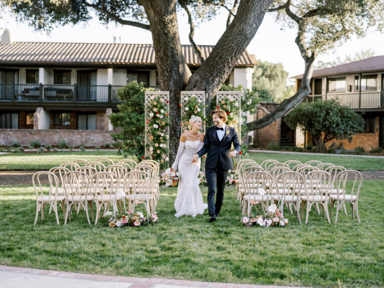 A bride and groom walking down the isle in a garden.