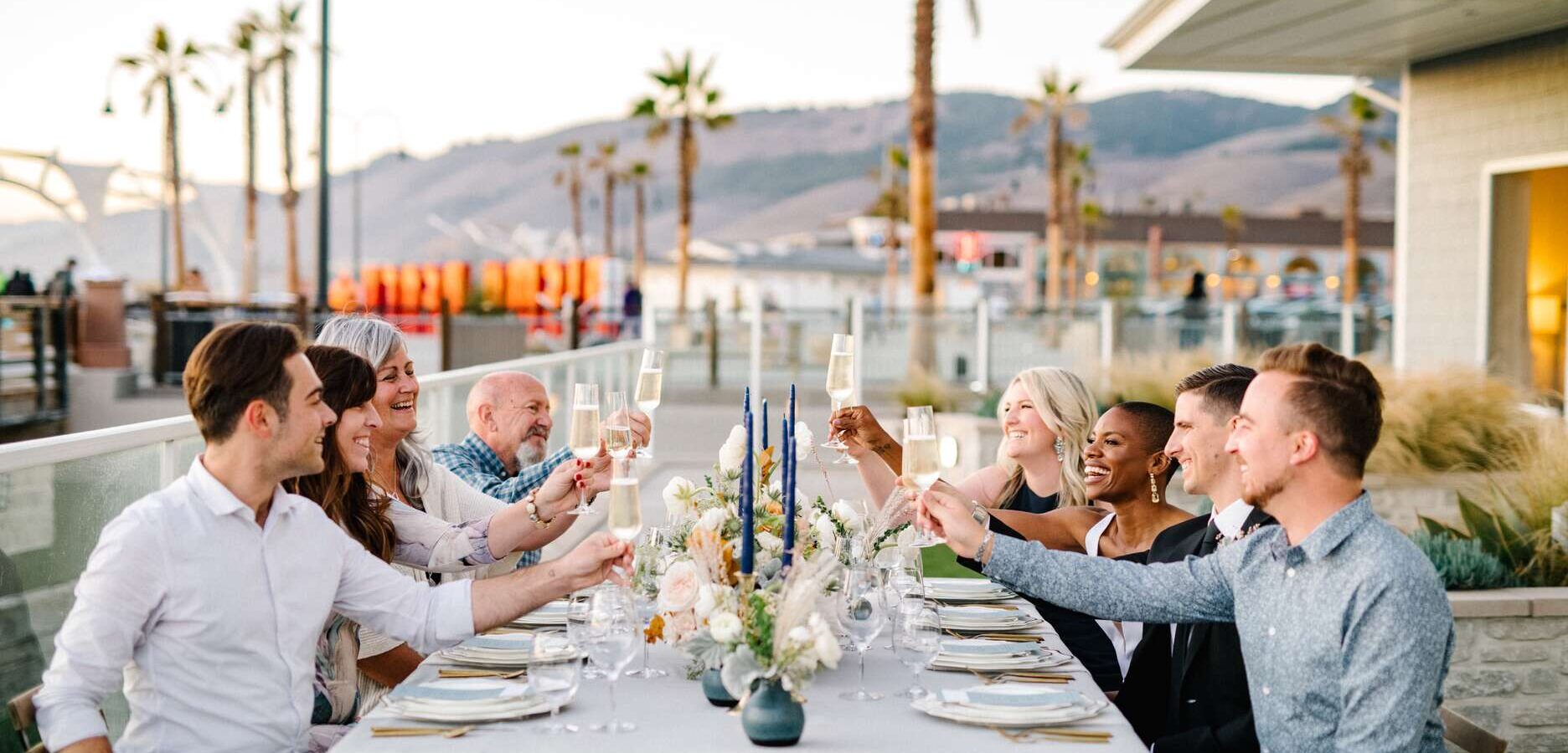 Group of people sitting outside raising their drinking glasses for a toast