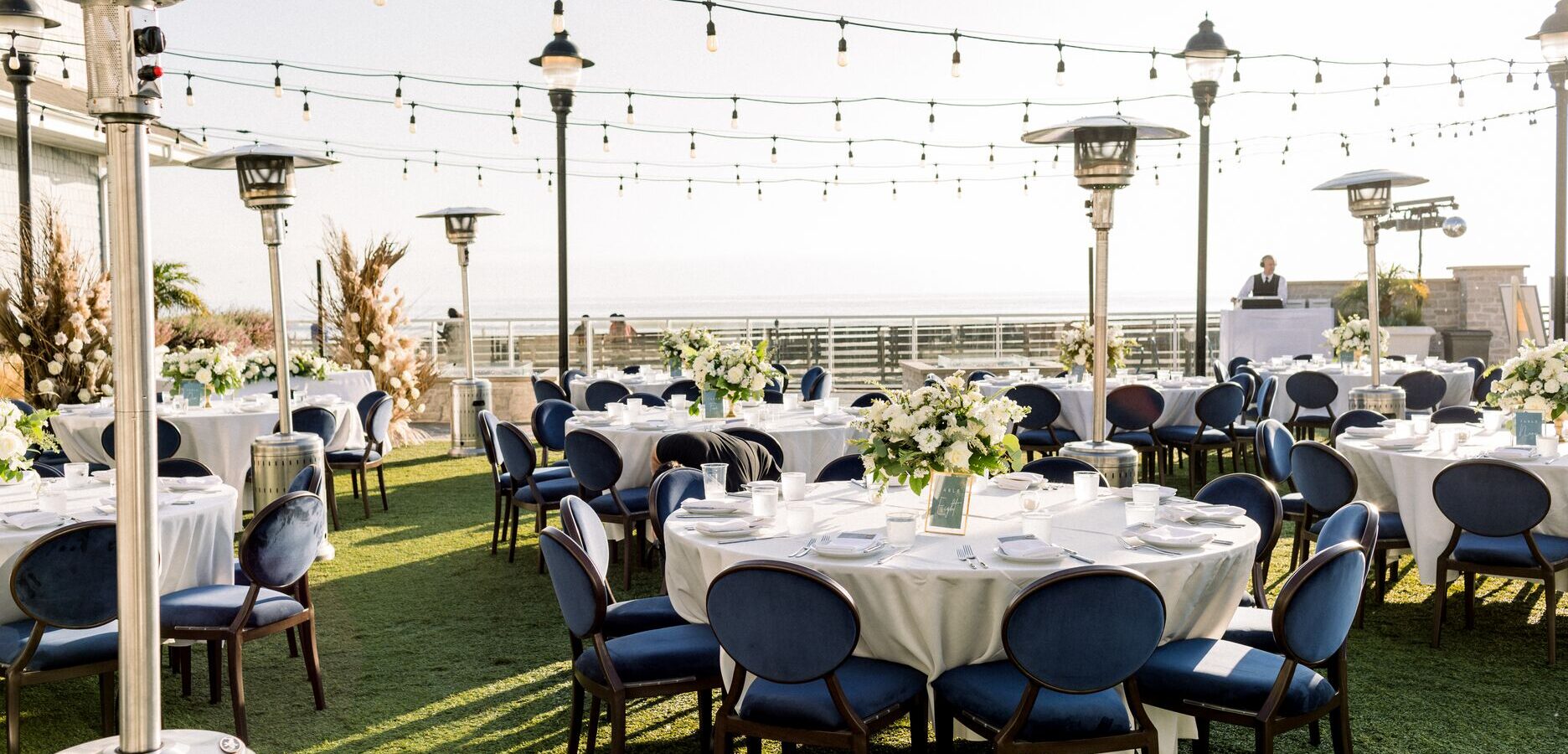 White table with blue chairs on lawn with string lighting overhead